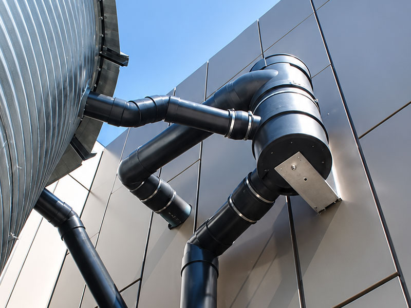 Black insulated industrial pipes and ducts mounted on a modern metal building exterior