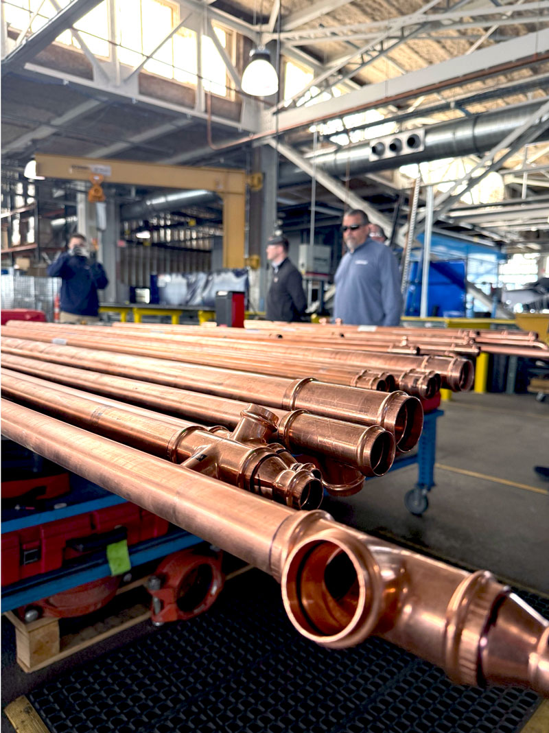 Copper pipes arranged on a workbench in a busy industrial workshop with workers in the background.
