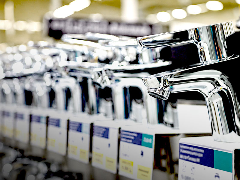 Chrome faucet handles on display in a showroom with a row of polished bathroom fixtures