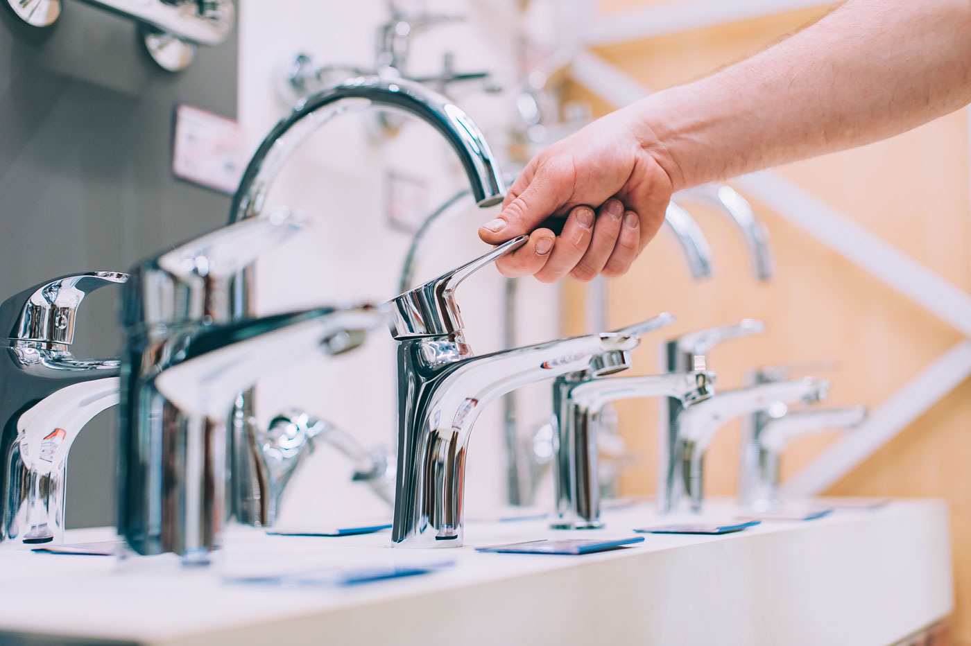 Close-up of a hand turning a shiny chrome faucet in a showroom display row of faucets