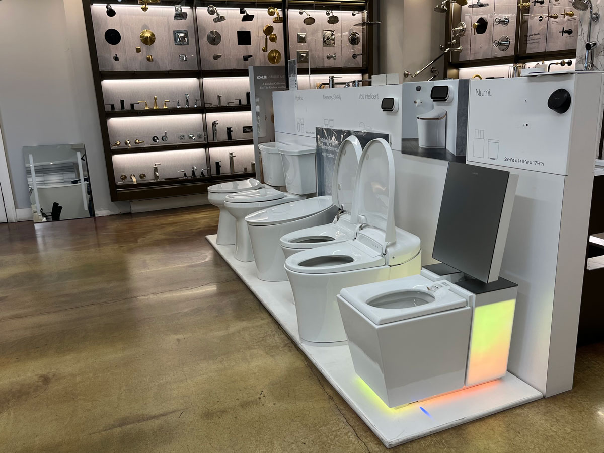 Row of white modern toilets on display in a showroom with faucet samples on the back wall