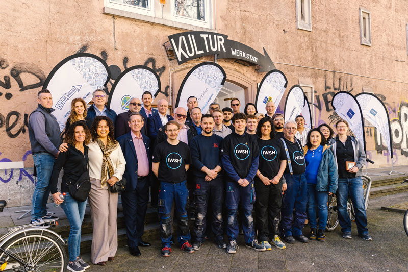 Group of people pose for a photo outside a building with 'KULTUR WERKSTATT' banners for a community event.