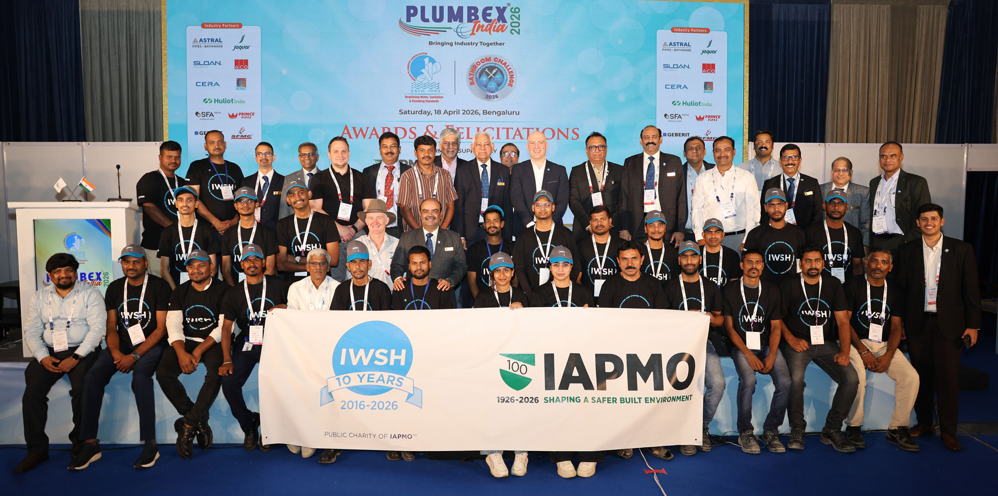 Group of attendees posing for a conference photo in front of a large event banner and side sponsor banners.